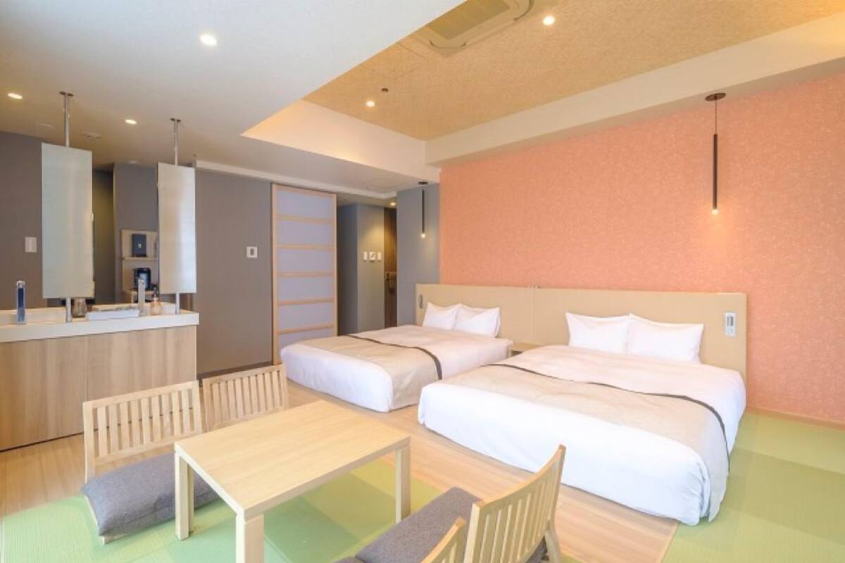 A hotel room with two beds, a small table, a bench, a desk, and a bathroom area.