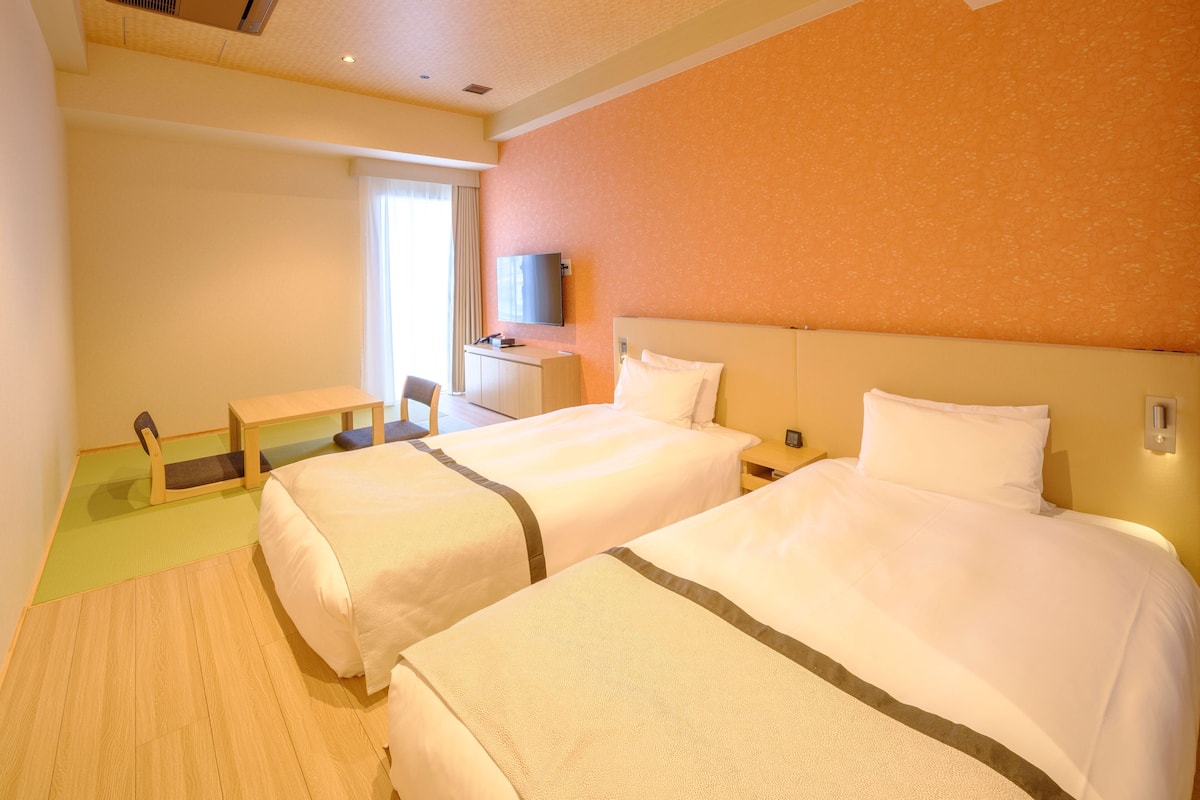 A hotel room with two beds, a desk, a chair, a television, and a window with curtains.
