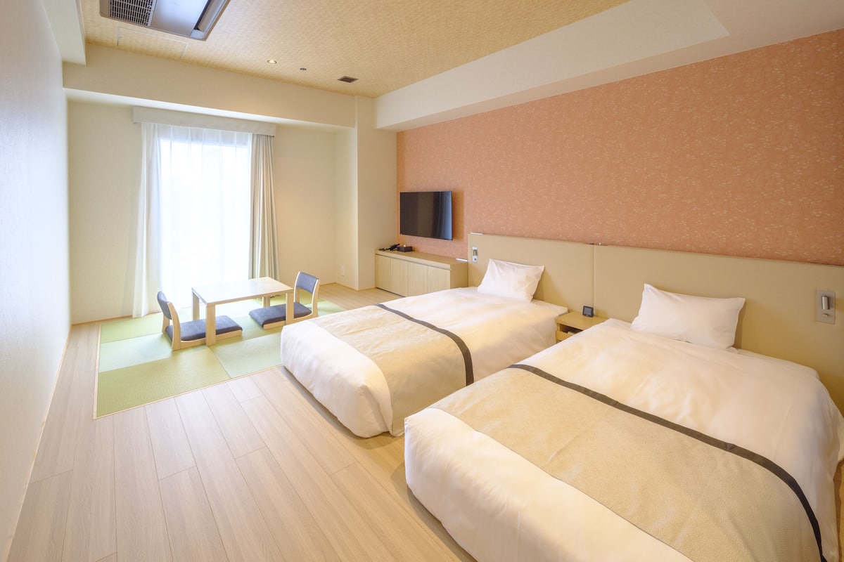 A hotel room with two beds, a TV, a desk, and a chair.
