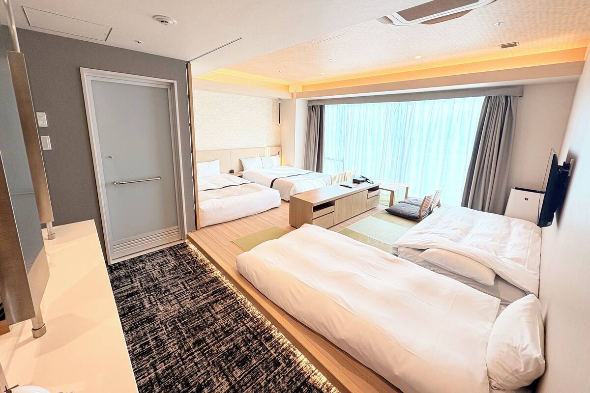 A hotel room with two beds, a desk, a chair, a small table, and a window with curtains.