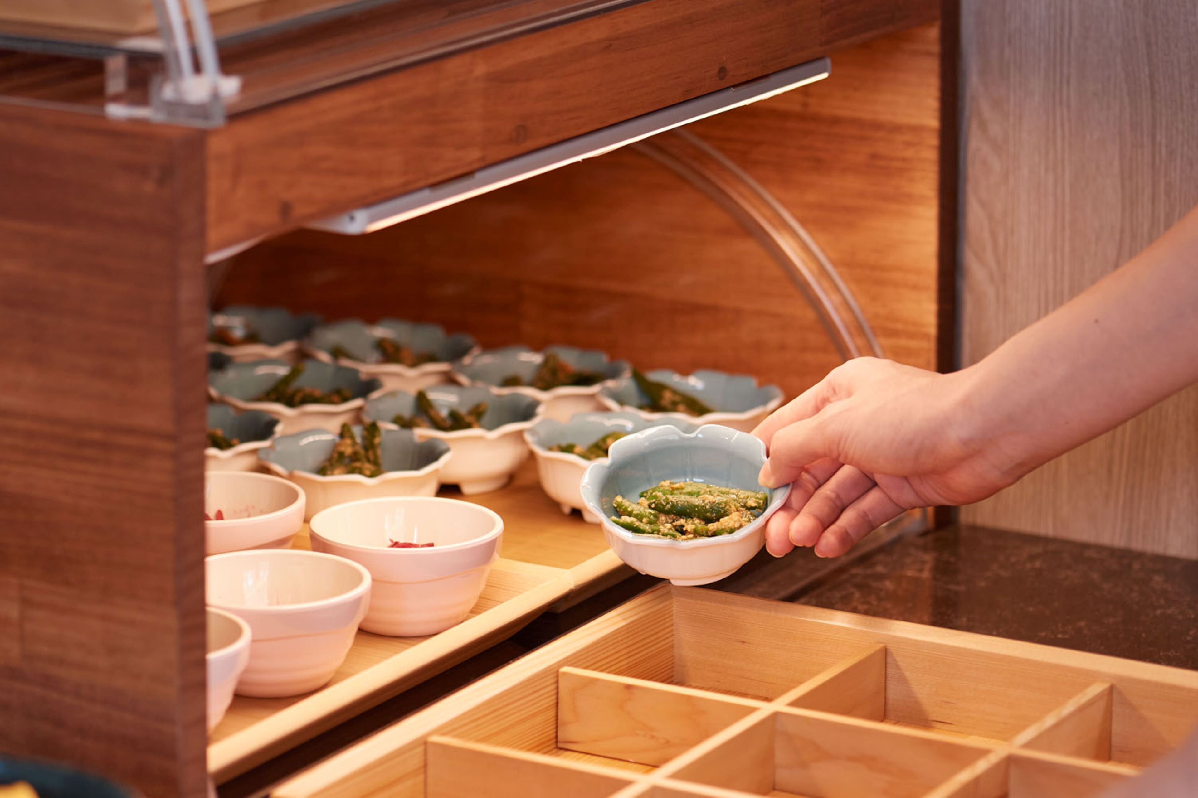 A hand holding a bowl with food, with multiple bowls and a wooden rack in the background.
