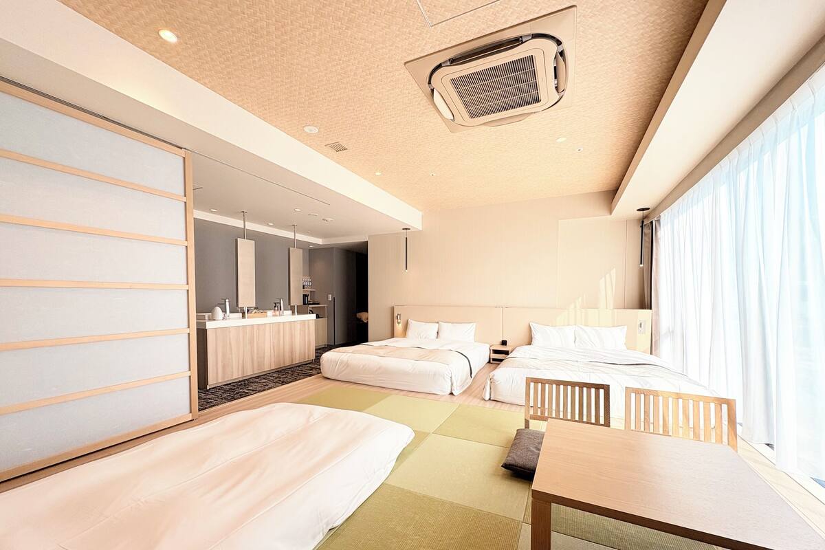 A modern hotel room with a large bed, a smaller bed, a desk, and a bathroom with a mirror and sink.