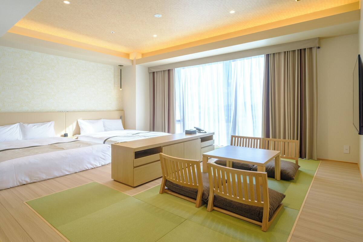 A hotel room with a bed, a desk, and a dining area with chairs and a table.