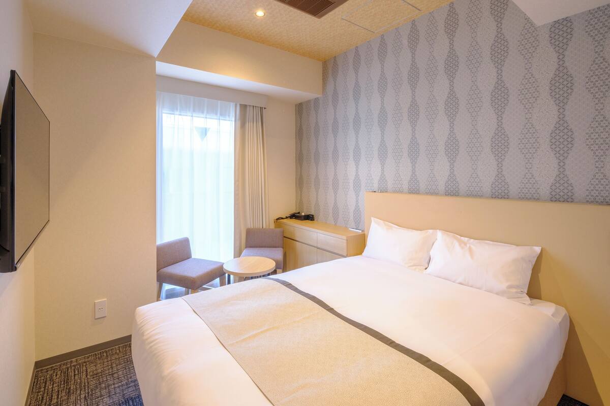 A hotel room with a large bed, a small desk, a chair, and a television.
