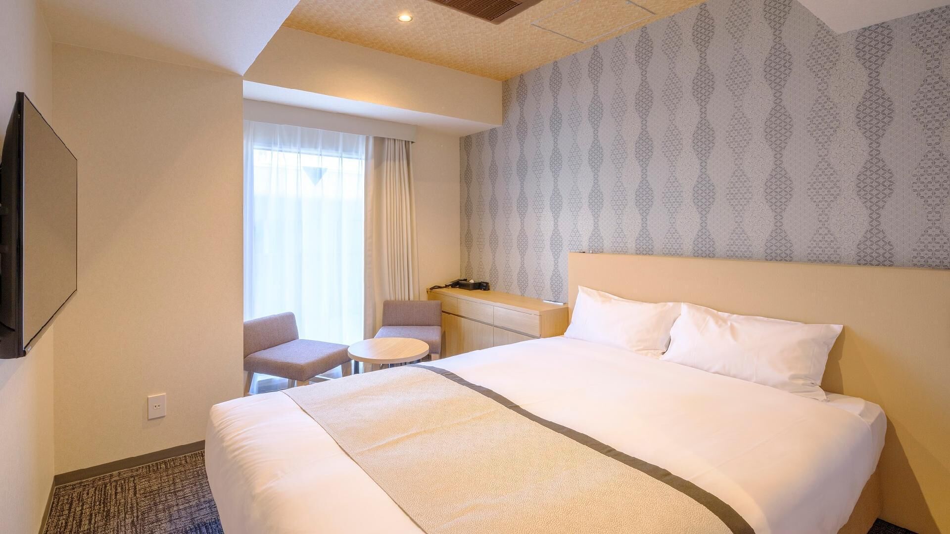 A hotel room with a large bed, a desk, a chair, and a television.