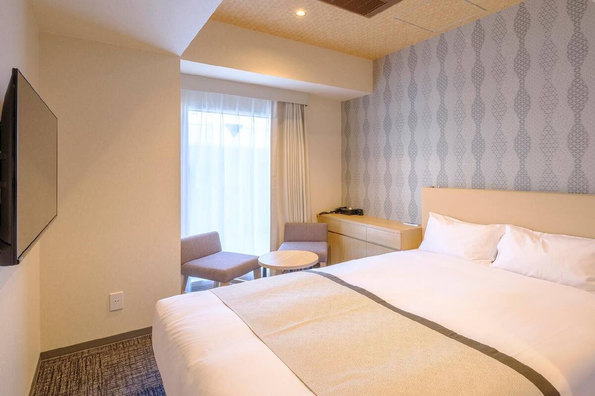 A hotel room with a large bed, a desk, a chair, and a television.