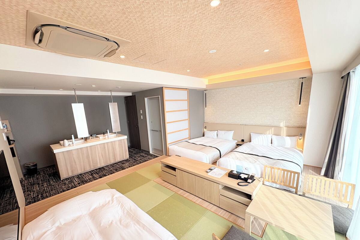 A modern hotel room with two beds, a small desk, a vanity, and a bathroom.