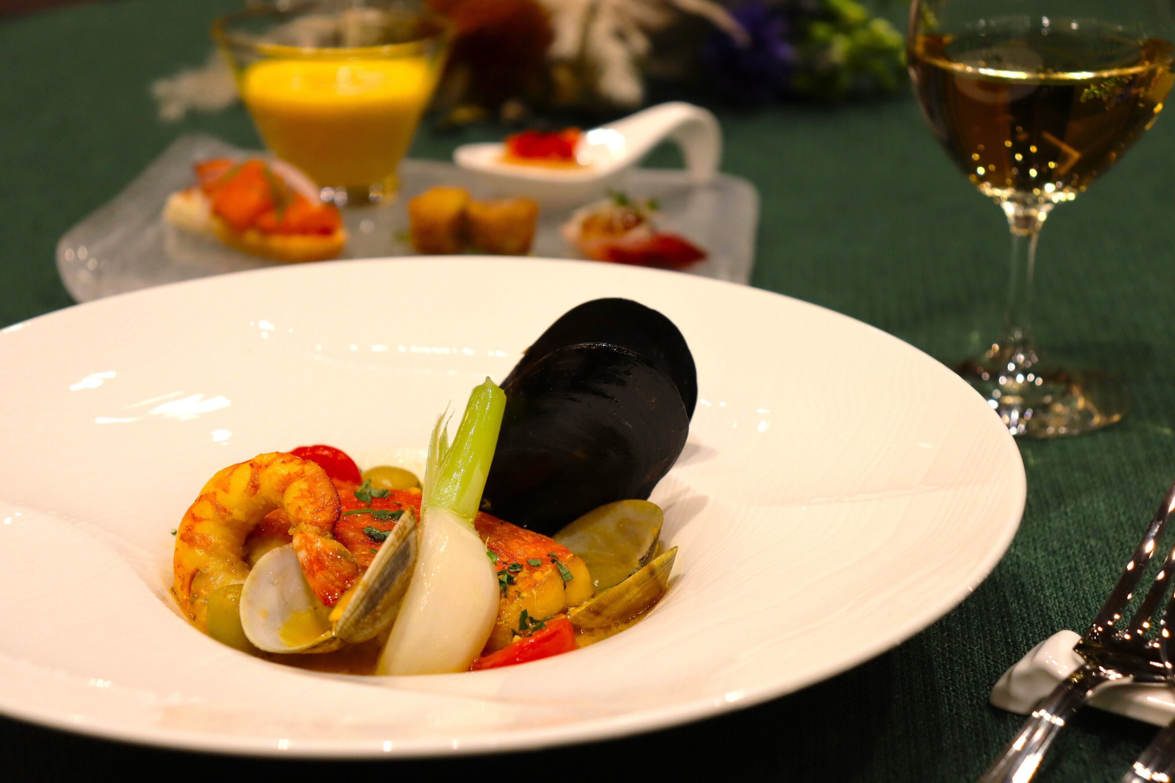 A seafood dish on a white plate with a glass of wine and a glass of orange juice in the background.