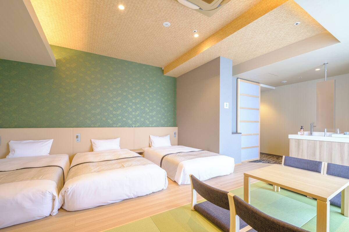 A hotel room with three beds, a dining table, and a kitchenette.
