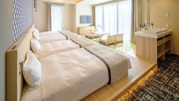 A hotel room with two beds, a desk, a chair, a large window, and a bathroom with a mirror and sink. - Tosei Hotel COCONE Tsukiji Ginza Premier (Tokyo)