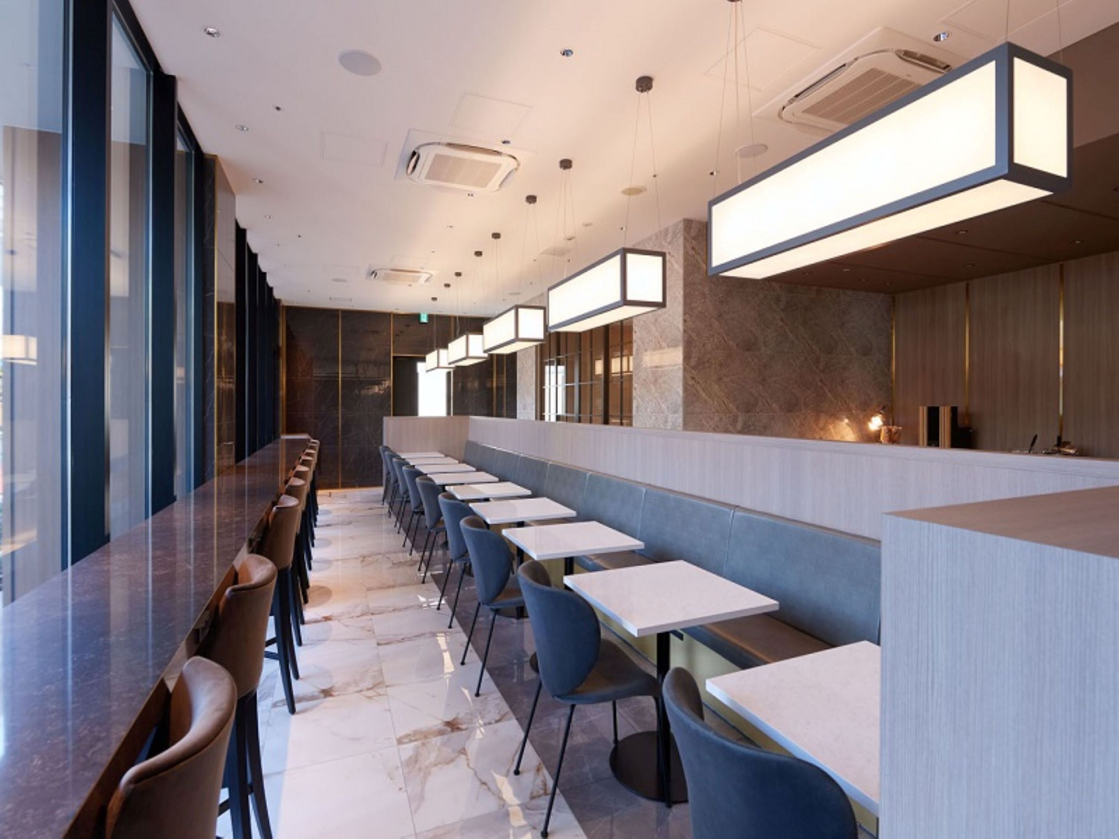A modern restaurant with a long counter, blue chairs, and white tables.