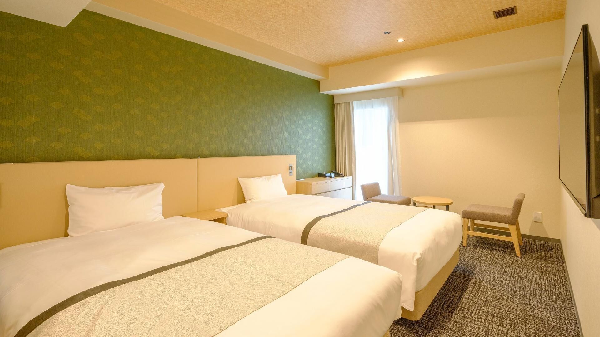 A hotel room with two beds, a small desk, a chair, and a TV.