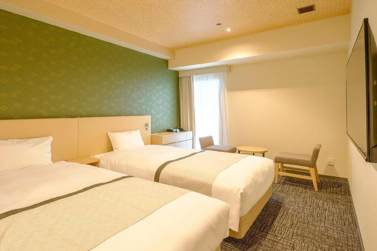 A hotel room with two beds, a small desk, a chair, and a TV.