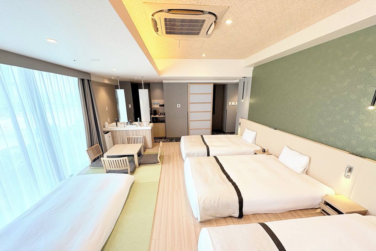 A hotel room with a large bed, a smaller bed, a desk, and a kitchenette.