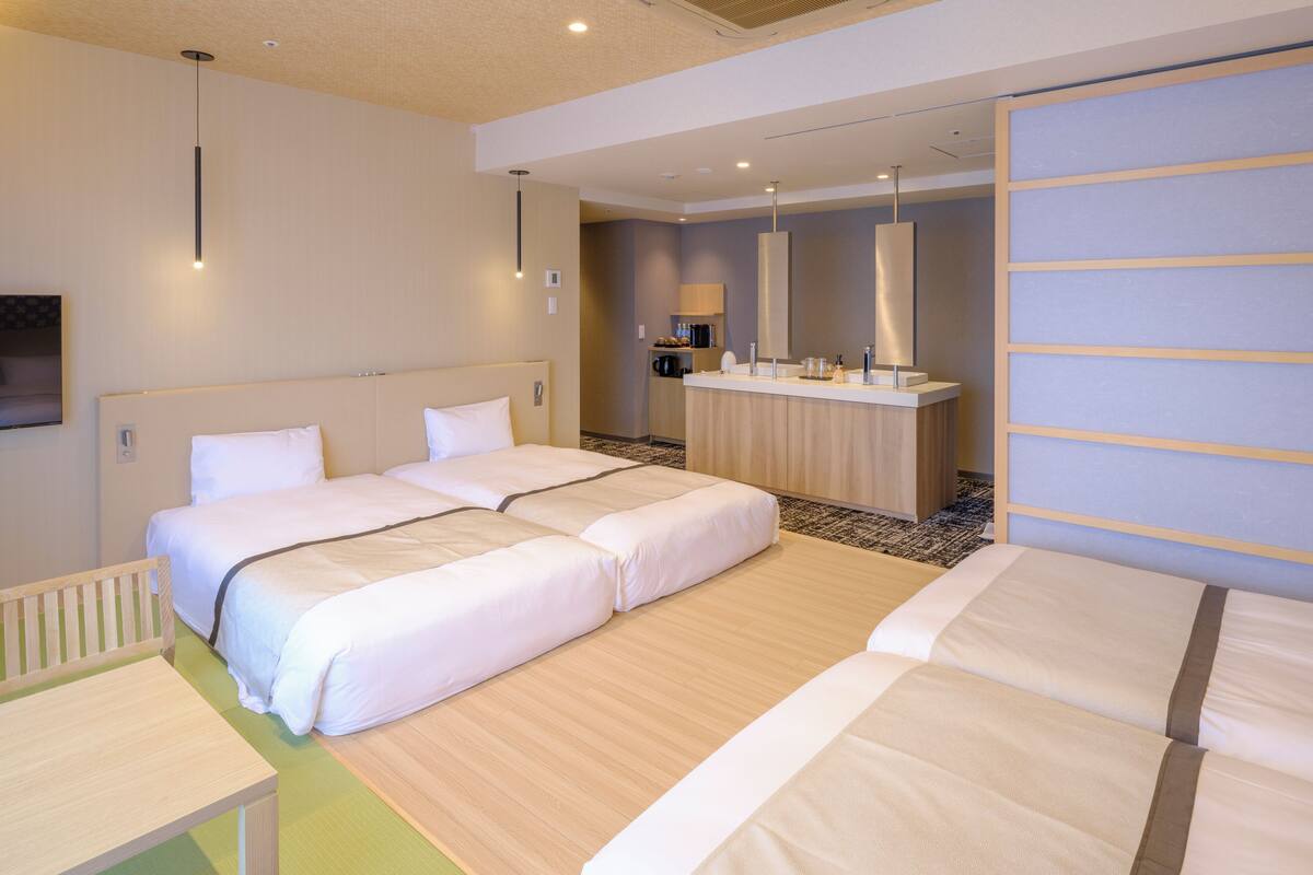 A hotel room with a large bed, a desk, and a kitchenette area.