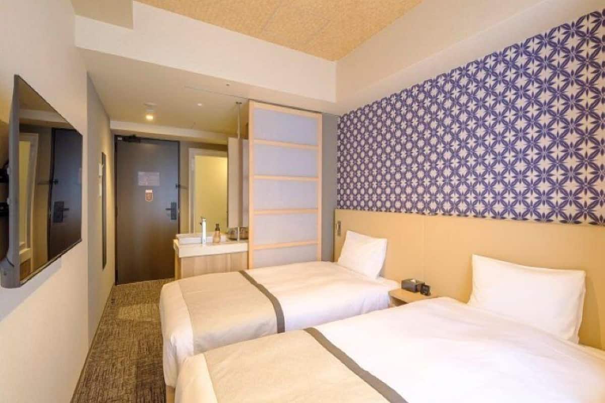A hotel room with two beds, a bathroom, and a patterned wall.
