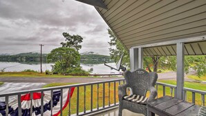 A covered porch with a view of a lake and hills, a wicker chair, and a table. - Northville Lakefront Escape w/ Deck: Walk to Lake (Northville)