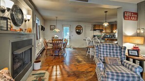 A cozy living room with a fireplace, dining area, and a kitchen in the background. - Northville Lakefront Escape w/ Deck: Walk to Lake (Northville)