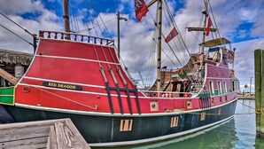 Ein großes, historisches Schiff liegt an einem Steg mit einem Holzboden, und ein Schild trägt die Aufschrift 'RED DRAGON'.