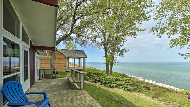 A wooden deck with blue chairs, a small gazebo, and a view of the water. - Lakefront Cottage Near Wineries + State Parks! (Mears)