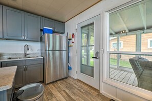 A compact kitchen with grey cabinets, a stainless steel refrigerator, a sink, and a window overlooking a wooden deck. - Lakefront Cottage Near Wineries + State Parks! (Mears)