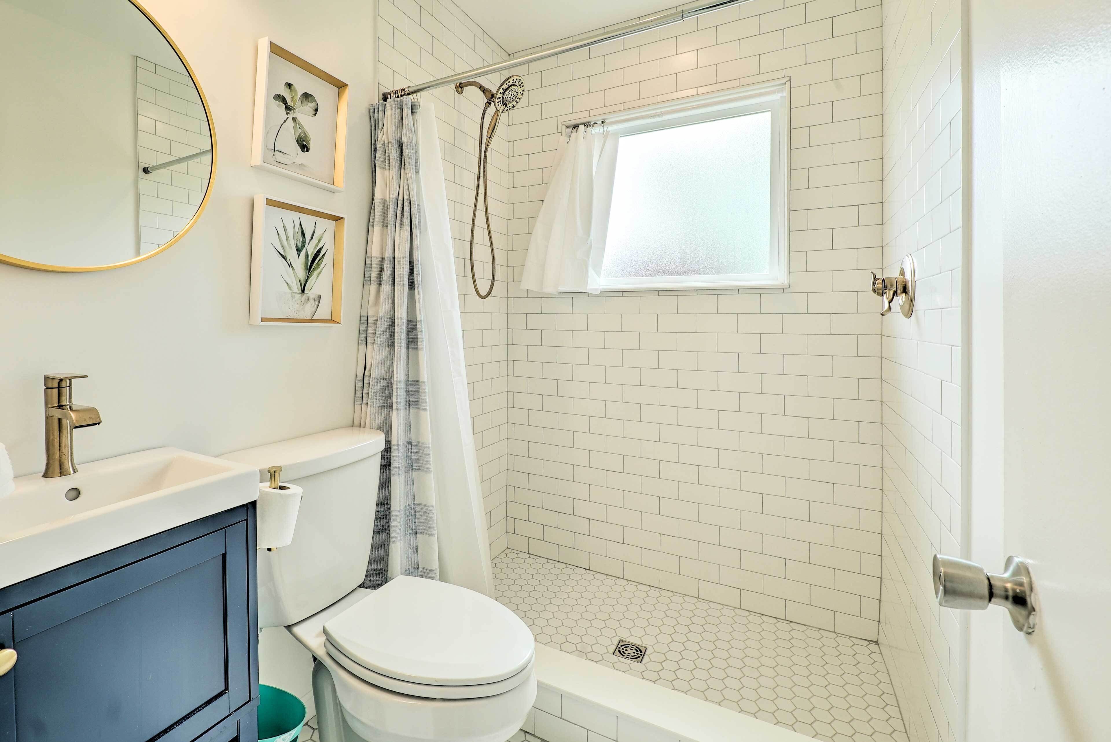 A bathroom with a white toilet, a sink, a mirror, and a shower area with a window.