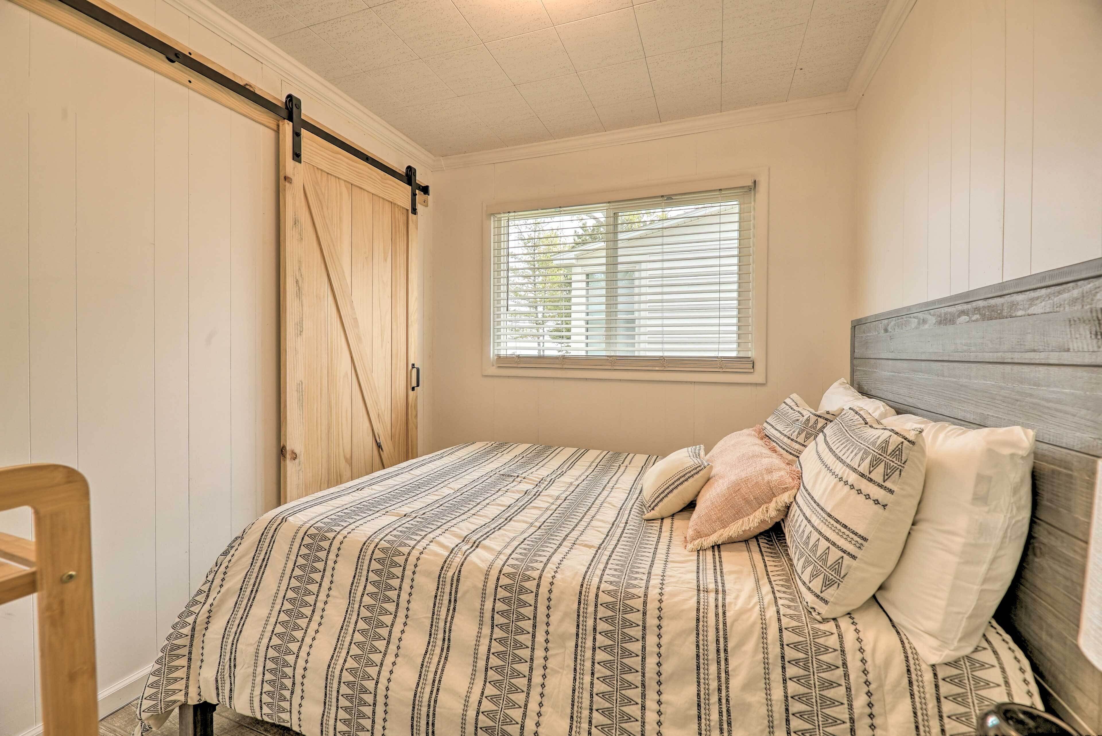 Une chambre à coucher avec un lit, une tête de lit en bois, une fenêtre avec des stores et une porte coulissante.