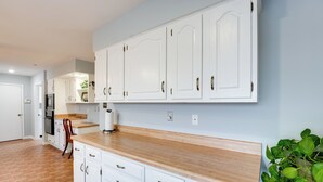 Une cuisine avec des meubles blancs, un plan de travail en bois et une plante.