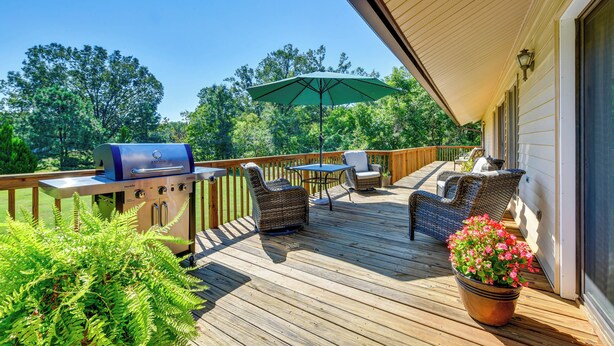 Une terrasse en bois avec un barbecue, des chaises en osier, une table et un pot de fleurs.