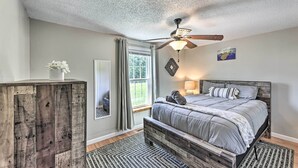 Une chambre à coucher avec un lit, un ventilateur de plafond, une fenêtre avec des rideaux et une commode en bois.