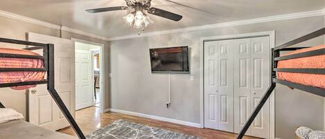 A bedroom with bunk beds, a ceiling fan, a TV mounted on the wall, and a door leading to another room.
