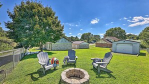 Un jardin avec un foyer en pierre, trois fauteuils Adirondack et un petit abri de jardin.