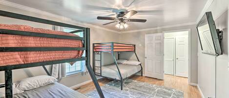 A room with bunk beds, a ceiling fan, a door, and a window.