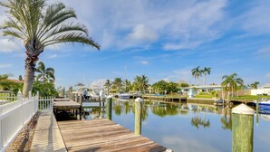 A wooden dock extending into calm water with a clear sky, surrounded by palm trees and a marina with boats. - Canal-front Haven: Pool, Dock & Lanai in Palmetto (Palmetto)