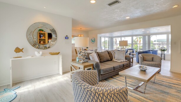 A spacious living room with a large window, a round mirror, and a white console table. - Canal-front Haven: Pool, Dock & Lanai in Palmetto (Palmetto)