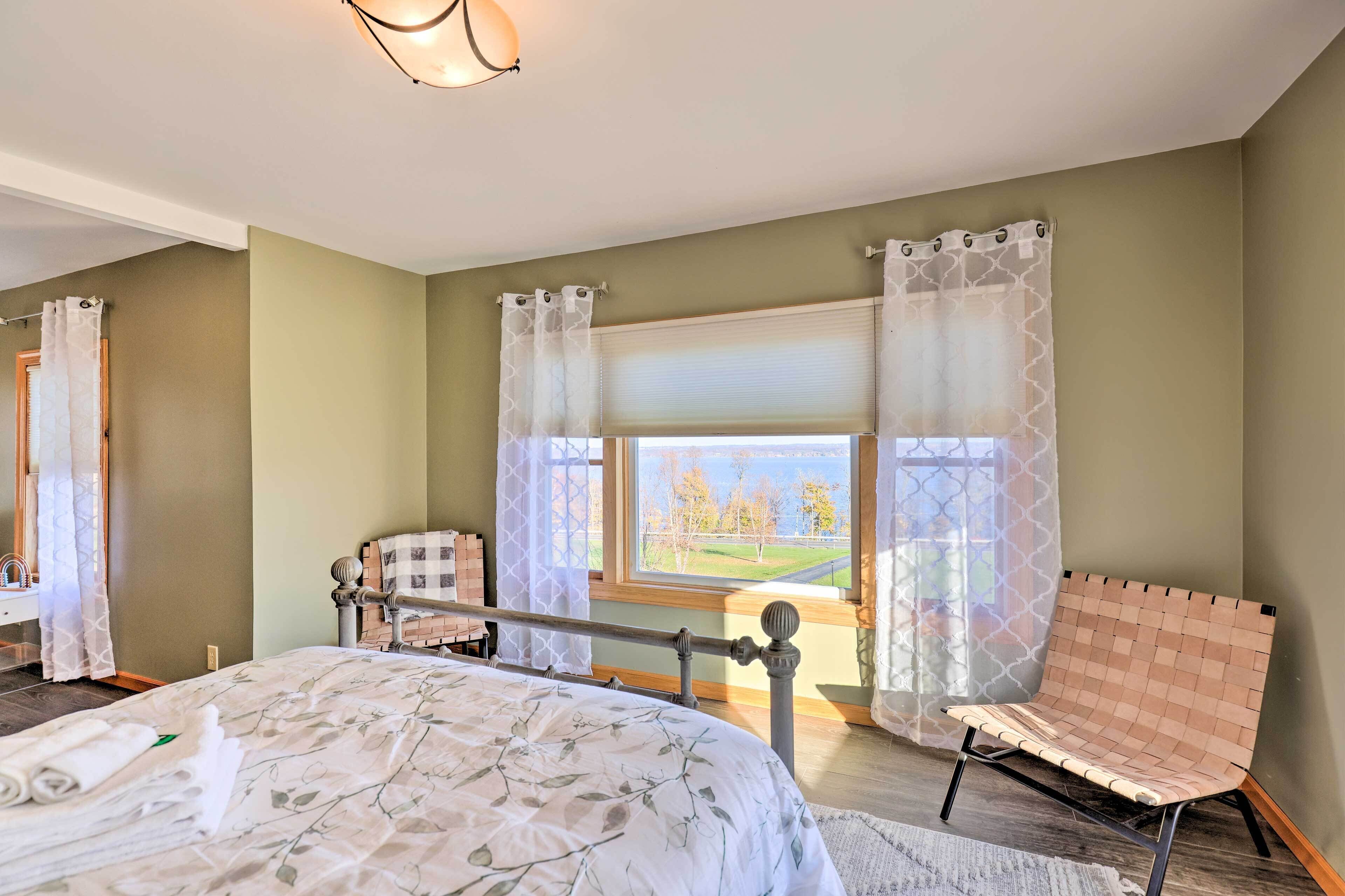 Une chambre à coucher comprenant un lit, une chaise, une fenêtre avec vue et une salle de bain avec un miroir et des rideaux.