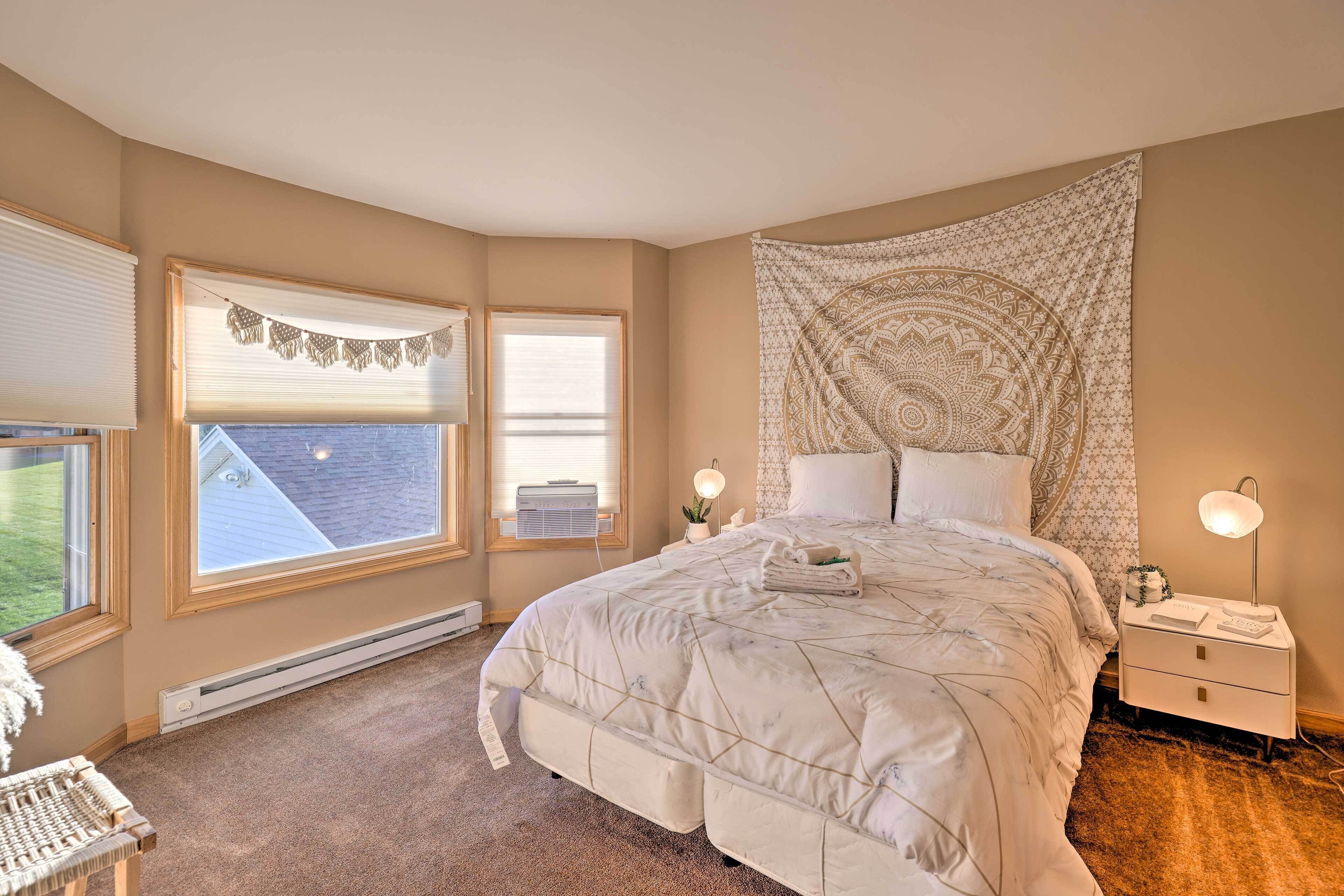 A bedroom with a large bed, two bedside lamps, a tapestry, and a window with blinds.