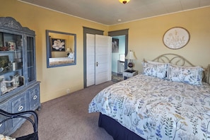 Quarto com cama, cômoda, espelho e porta que dá para outro ambiente.