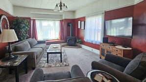 Een woonkamer met een bank, een tafel, een televisie, een open haard en een plant.