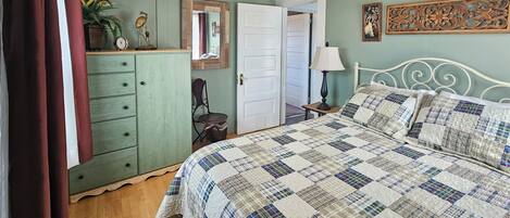 A bedroom with a bed, dresser, mirror, lamp, and a door leading to another room.