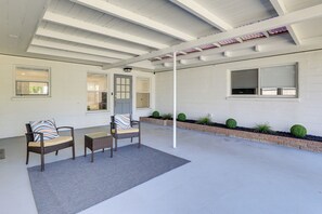 Un patio techado con dos sillas de mimbre, una mesita y un tapete gris.