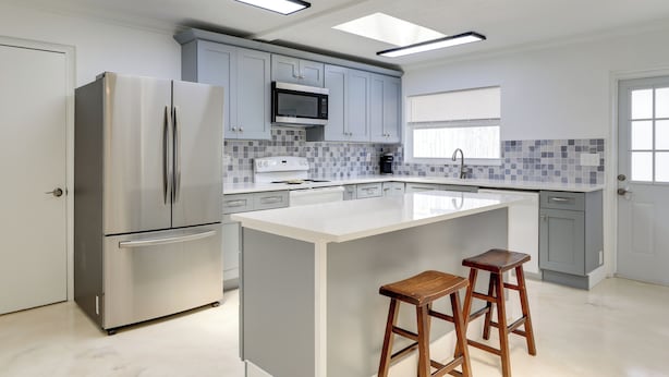 A modern kitchen with a stainless steel refrigerator, a microwave, and a large island with two wooden stools. - Dog-friendly Home w/ Patio & BBQ in Bradenton (Bradenton)