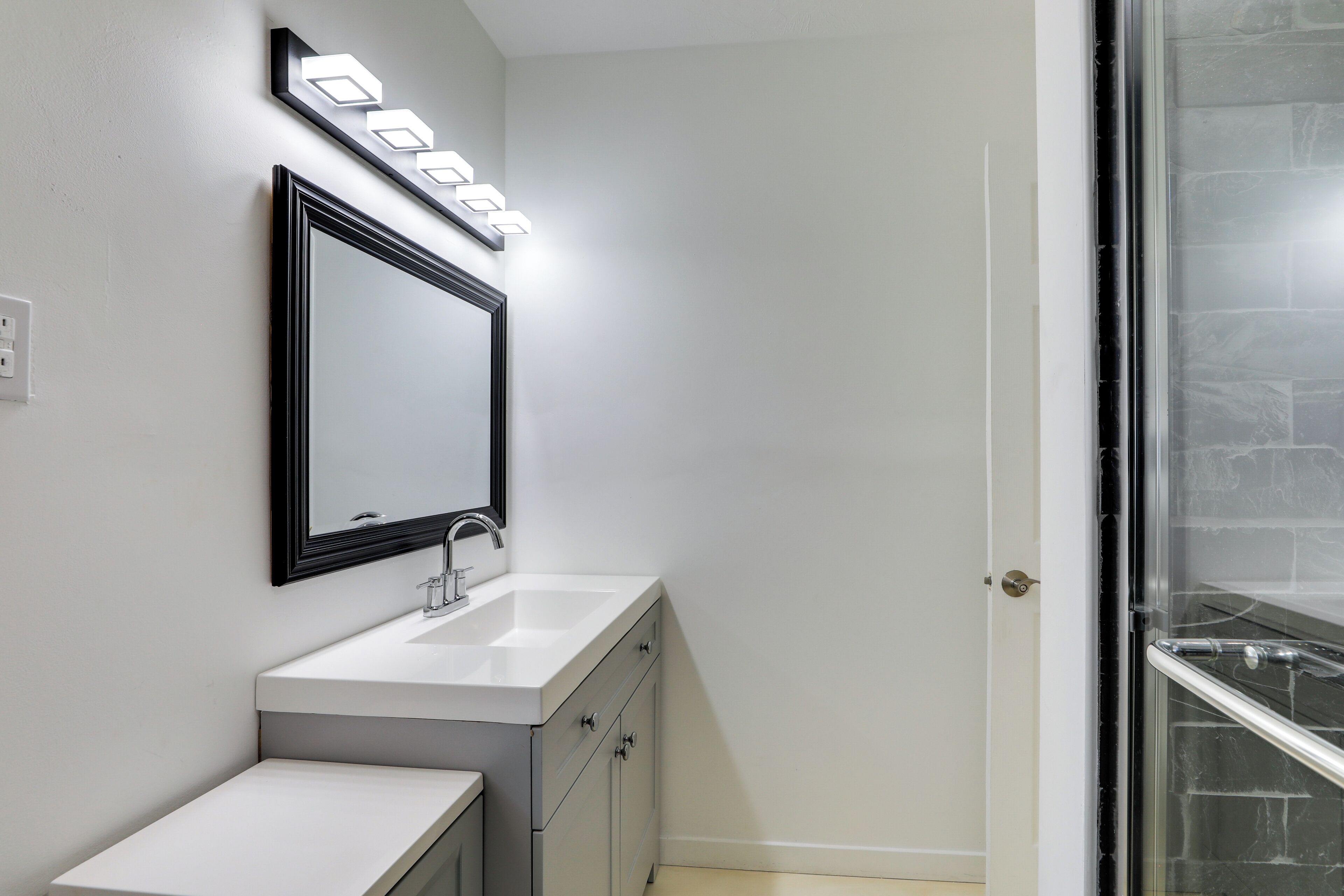 A bathroom with a white sink, a black-framed mirror, and a shower with a glass door.