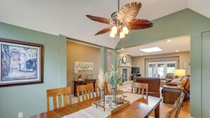 A dining area with a wooden table, chairs, and a ceiling fan. There is a fireplace in the background and a painting on the wall. - Bella Vista Home w/ Kayaks & Deck on Loch Lomond! (Bella Vista)