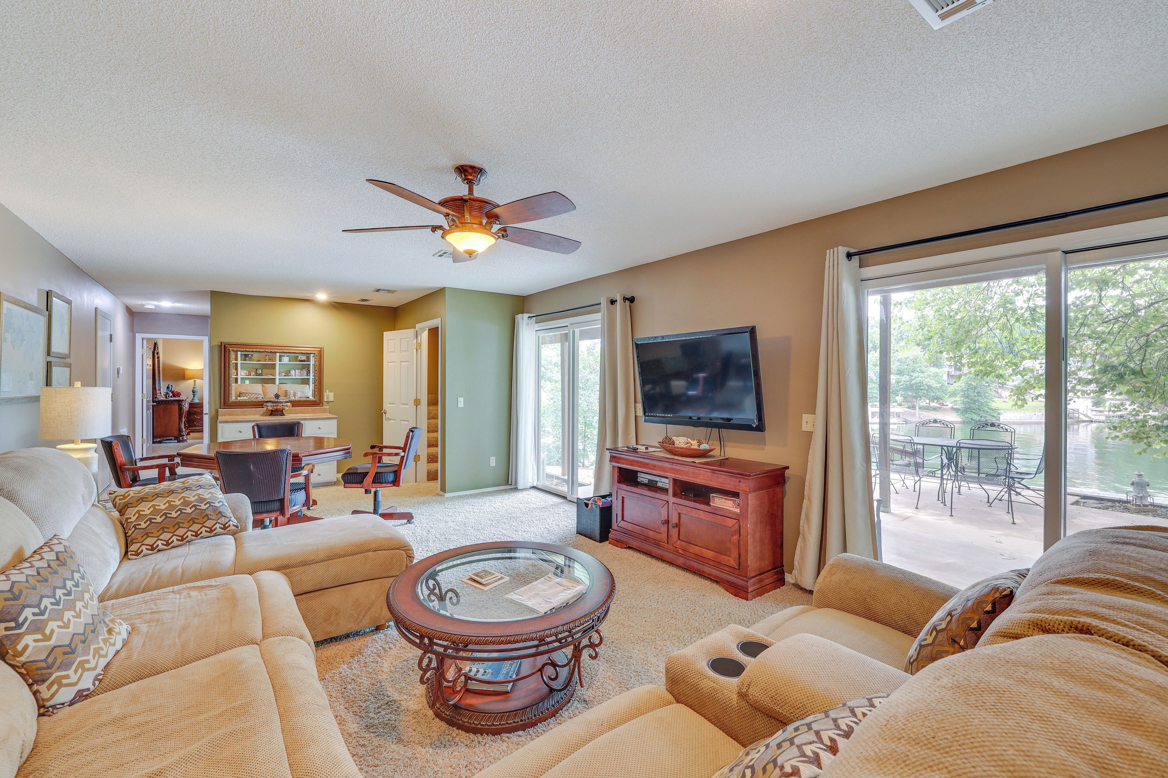 A living room with a ceiling fan, a glass coffee table, sofas, a TV, and a view of a patio with outdoor furniture.
