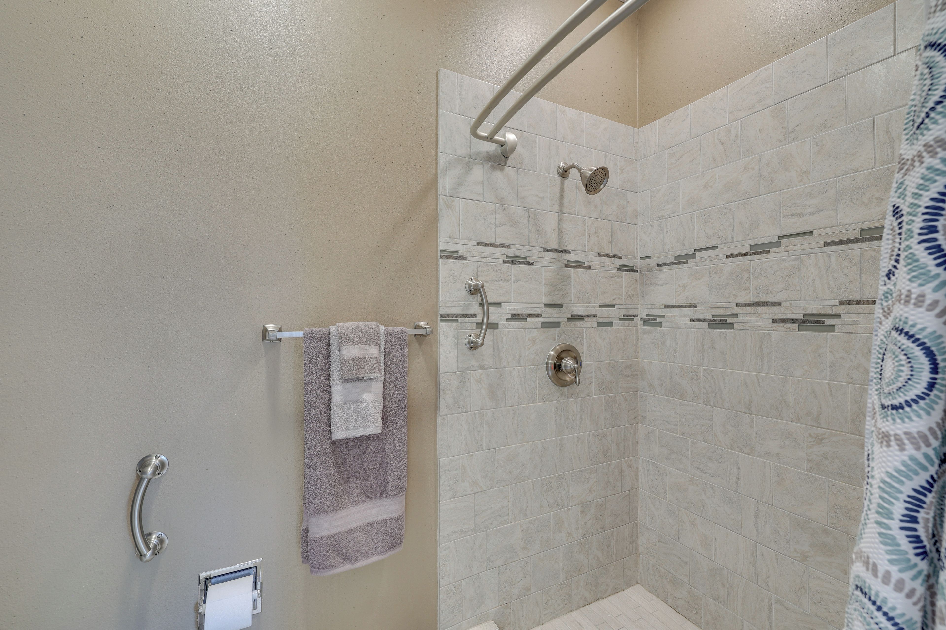 A shower with a handrail, a towel rack with a towel, and a toilet paper holder.