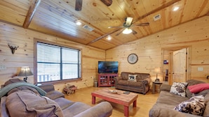 A log cabin interior with a wooden ceiling, a ceiling fan, a television, and two couches. - Broken Bow Cabin w/ Hot Tub & Covered Deck! (Broken Bow)