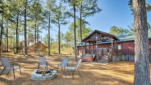 A cabin with a covered porch, a fire pit, and two chairs. - Broken Bow Cabin w/ Hot Tub & Covered Deck! (Broken Bow)