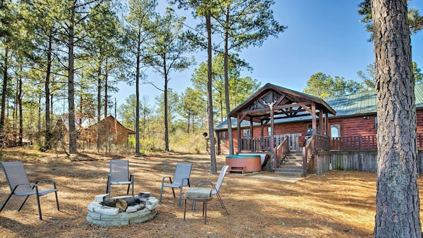 A cabin with a covered porch, a fire pit, and two chairs. - Broken Bow Cabin w/ Hot Tub & Covered Deck! (Broken Bow)