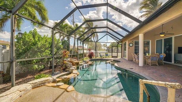 A covered outdoor swimming pool with a glass ceiling, surrounded by palm trees and a patio area with outdoor furniture. - Spacious Oasis w/ Lagoon Pool & Spa in Cape Coral! (Cape Coral)
